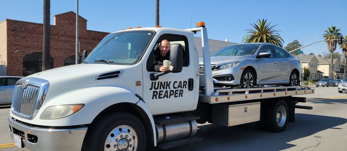 Junk Car Reaper driver holding cash out the window while towing a vehicle in San Jose